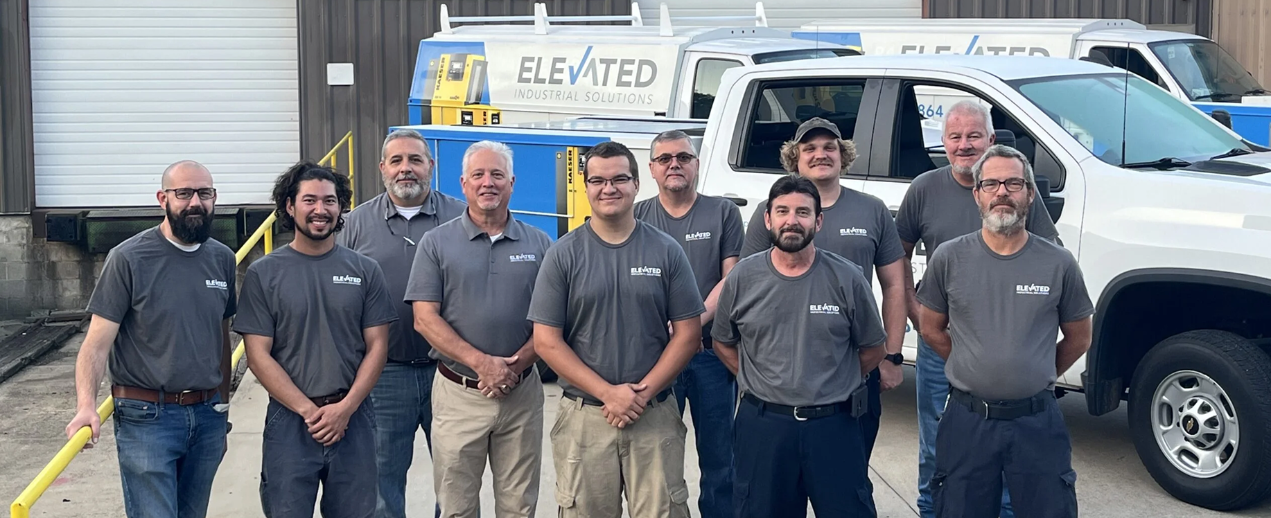 Team of Elevated Industrial Solutions employees standing together outside in front of company vehicles, with overlay text reading “About Elevated Industrial” and an “About Us” button. 